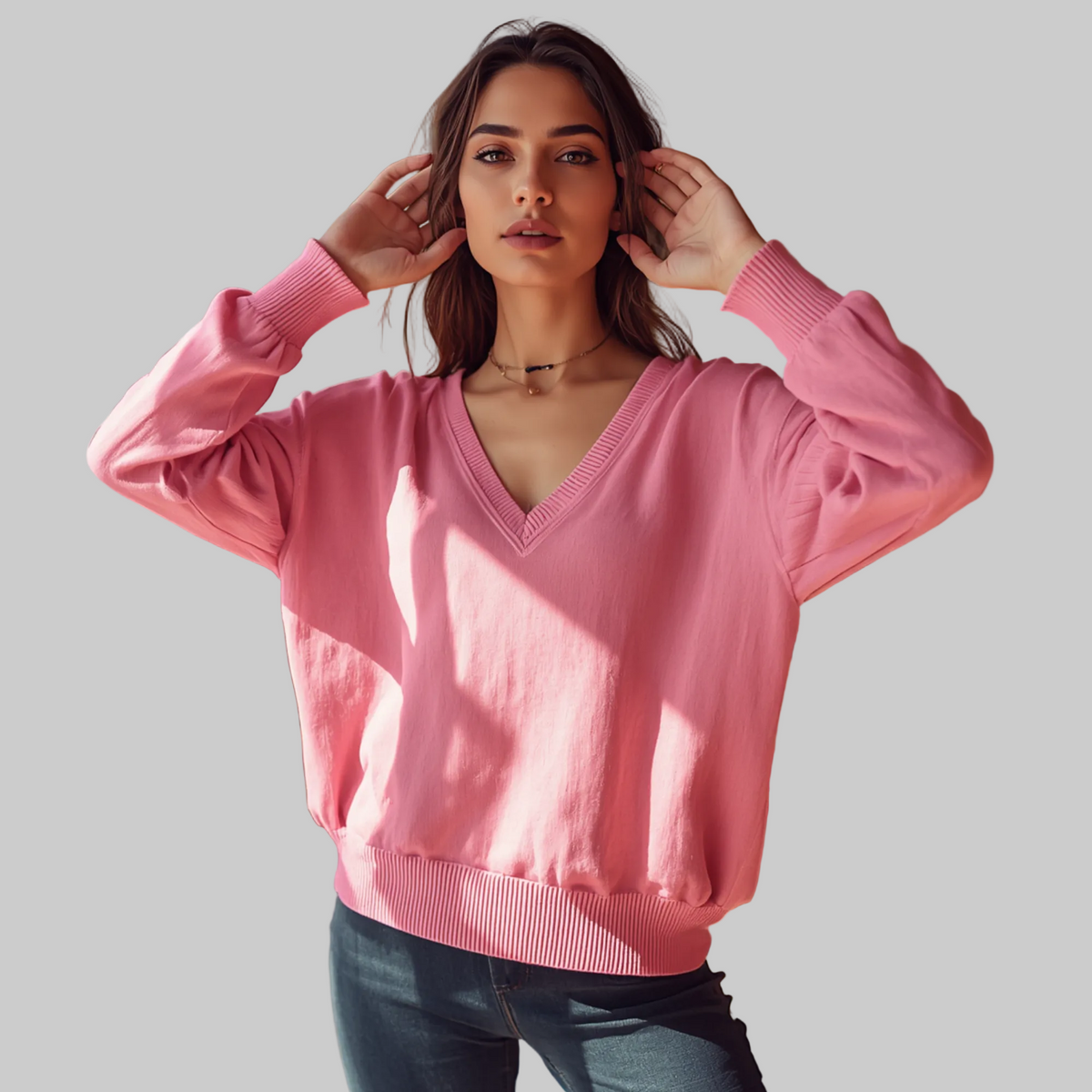Frau trägt einen rosa Pullover mit V-Ausschnitt, langen Ärmeln und Bündchen zu dunklen Hosen in einem Café.