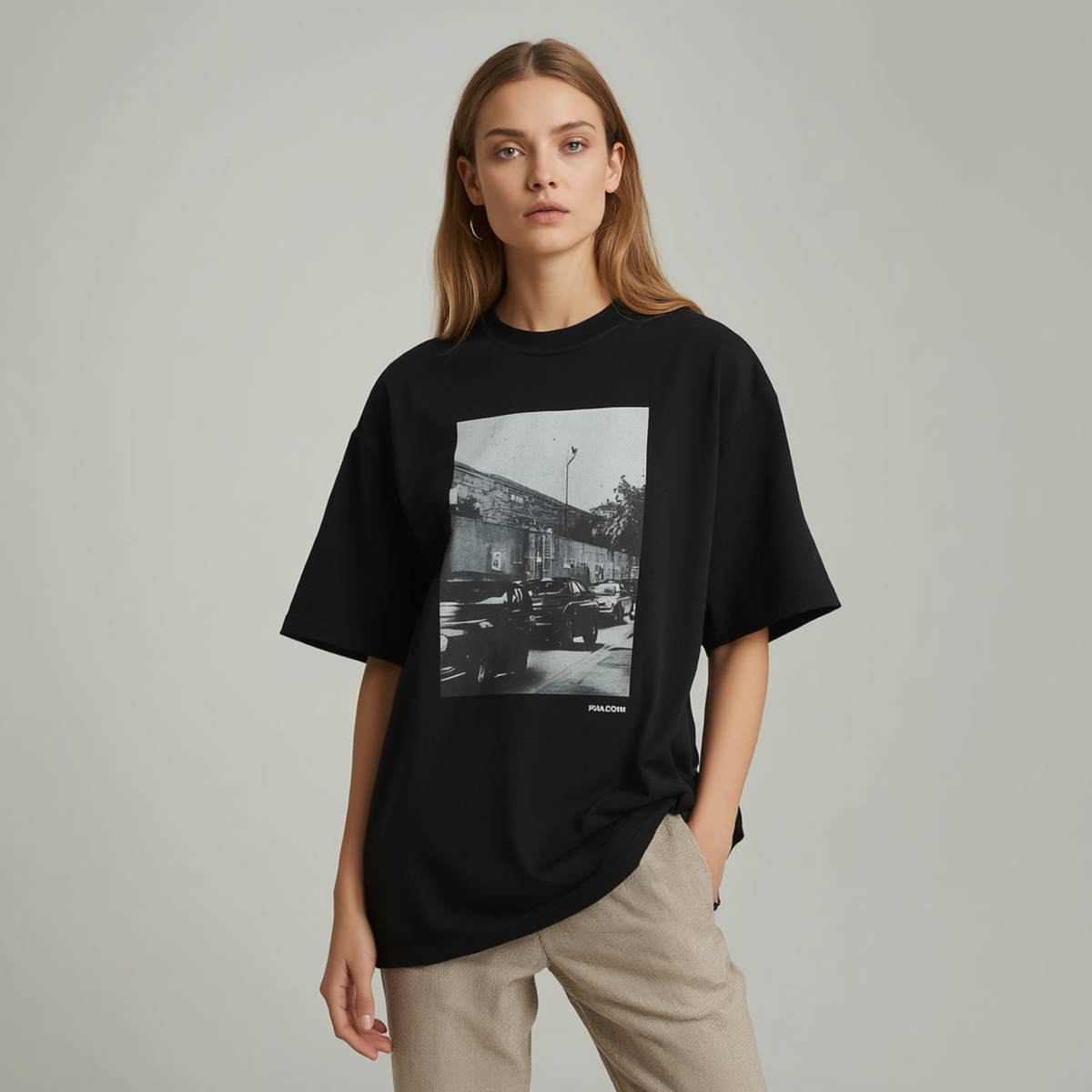Frau trägt ein schwarzes Oversize T-Shirt mit quadratischem Schwarz-Weiß-Straßenszenen-Druck und hellgrauen Hosen.